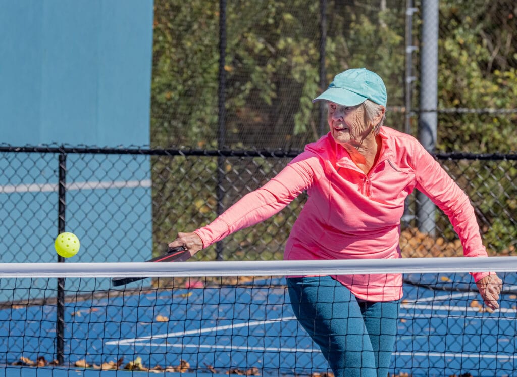 Senior Woman Strikes A Sliced Backhand Volley During Pickleball
